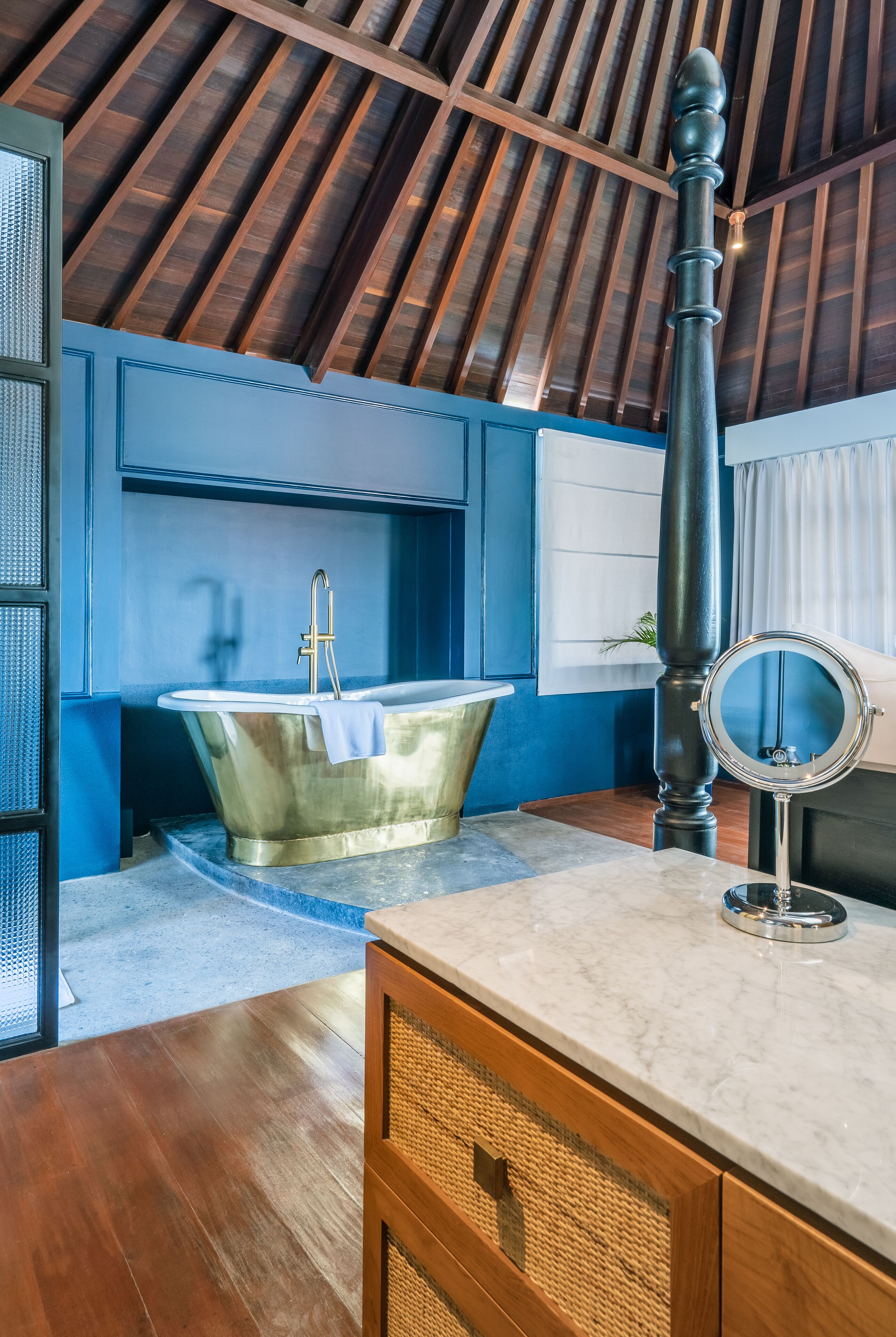 A bathroom with a freestanding bathtub, a vanity with a mirror, and a wooden ceiling.