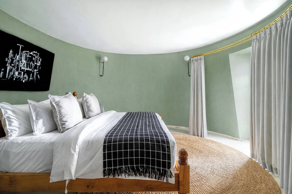 A bedroom with a bed, a wall-mounted artwork, two wall sconces, and a window with curtains.