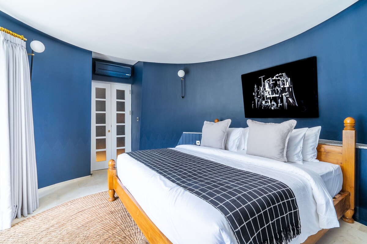 Un dormitorio con una cama, una obra de arte en la pared, una lámpara en el techo y una puerta.