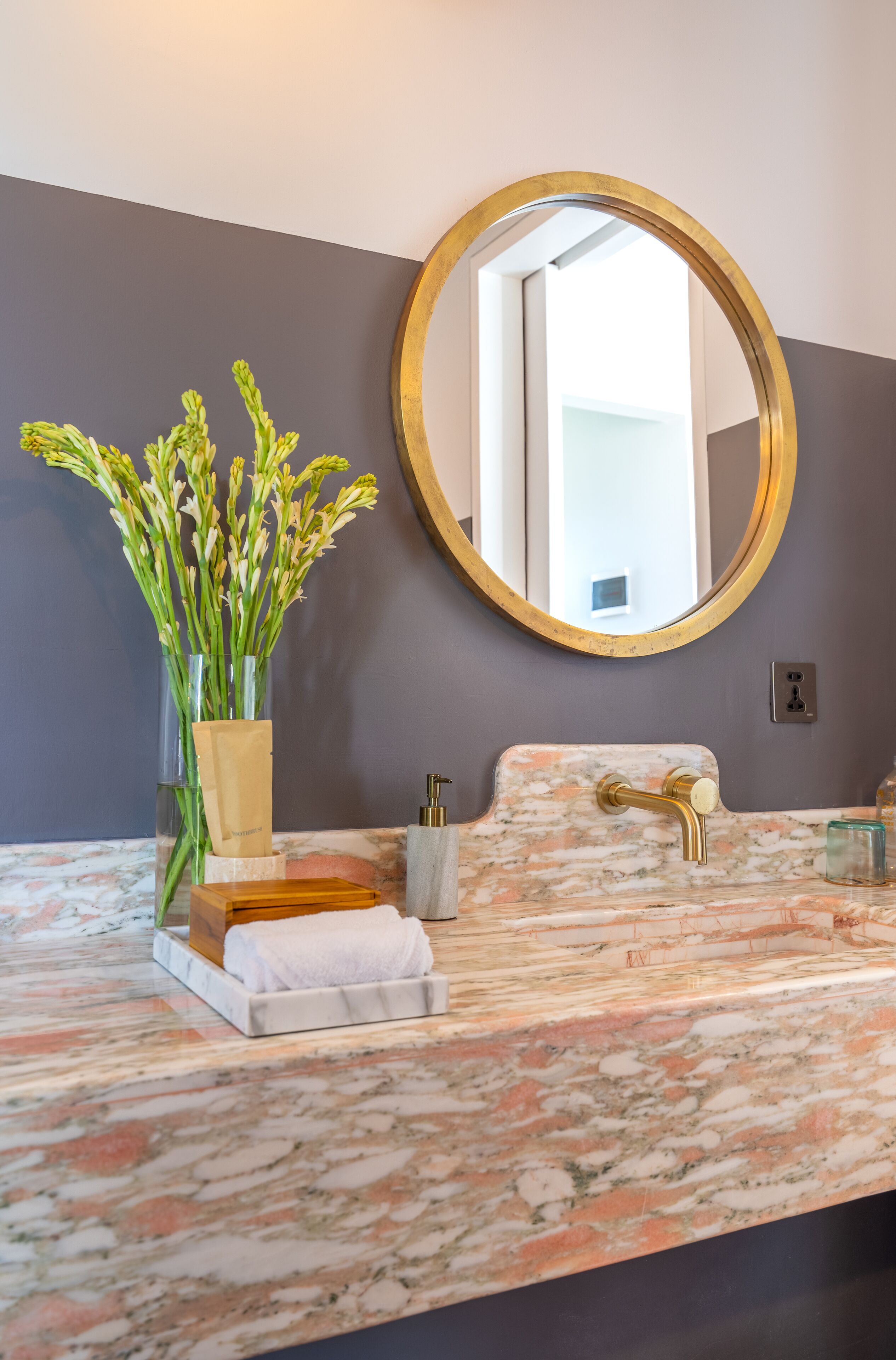 A bathroom with a marble sink, a gold-framed mirror, and a vase of flowers.
