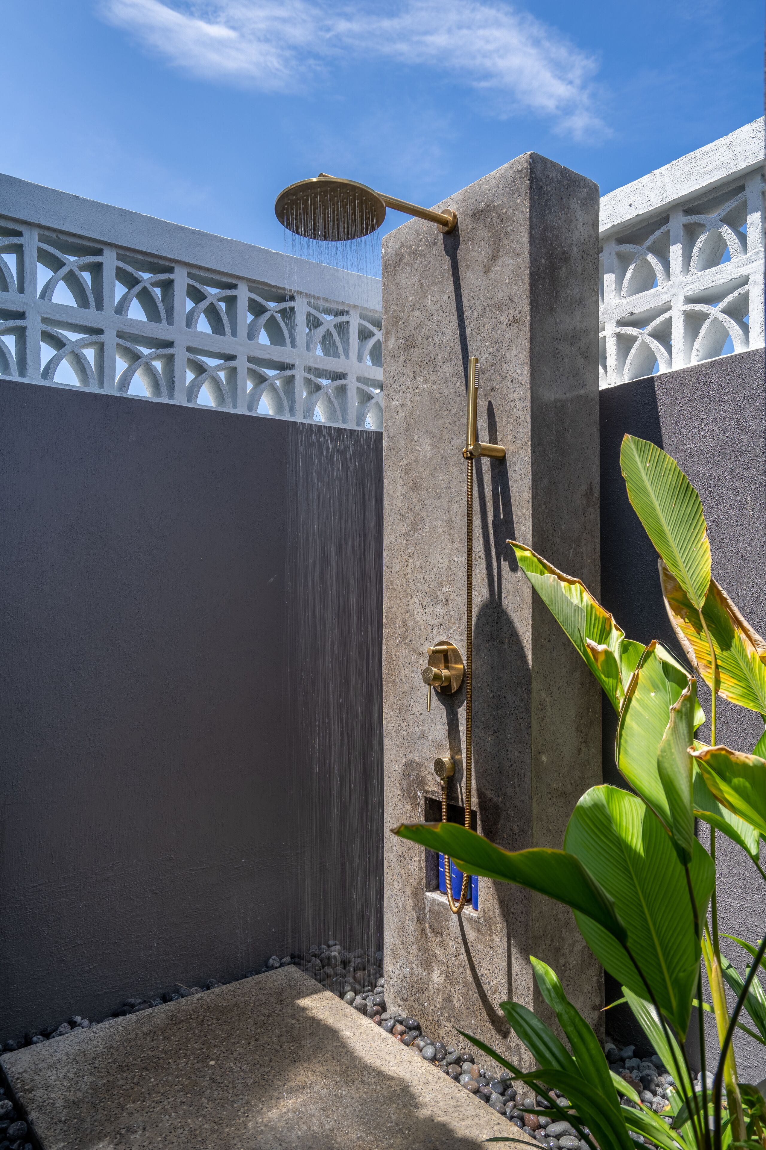 A concrete shower enclosure with a rain showerhead, a small window with blue trim, and a white decorative fence.