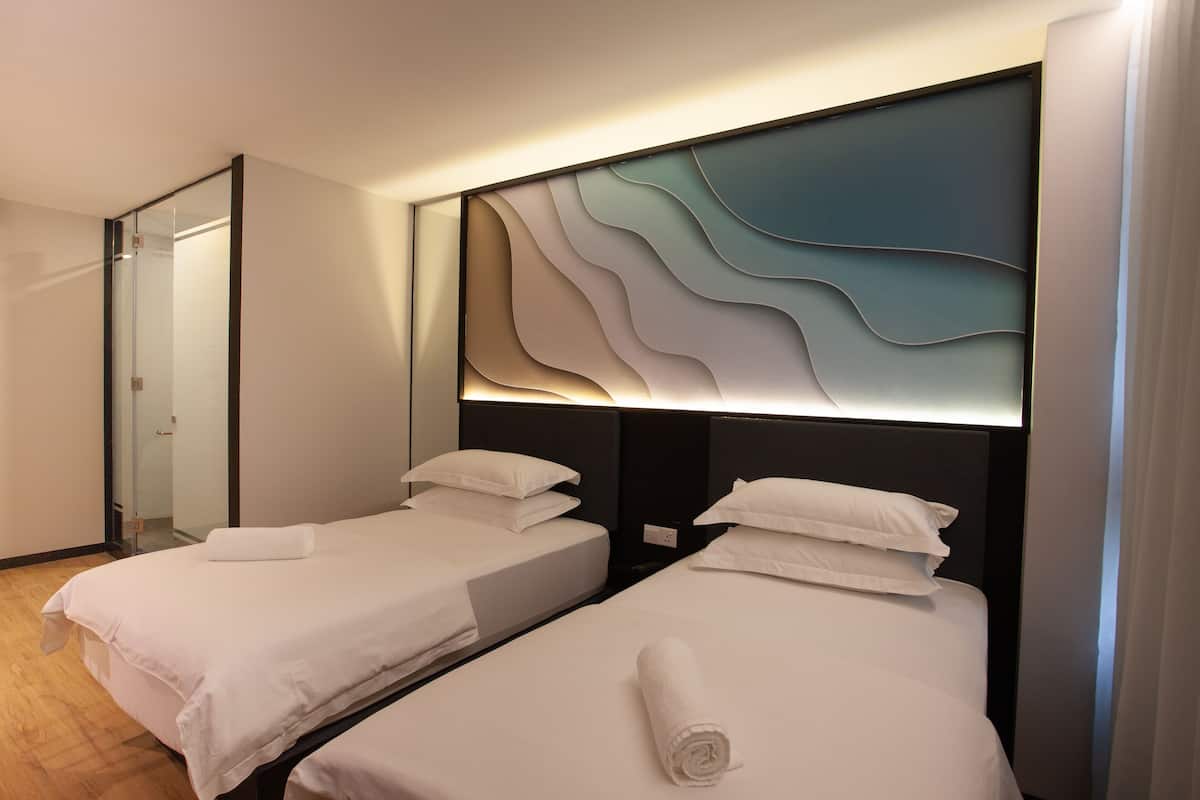 Ein Hotelzimmer mit zwei Betten, einem modernen Kopfteil und einer Glastür zum Badezimmer.