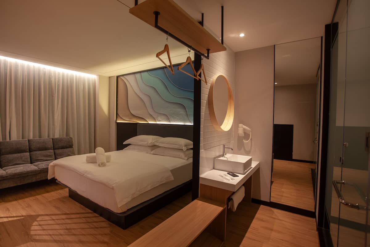 Ein modernes Hotelzimmer mit einem großen Bett, einer Couch, einem Schminktisch mit Spiegel und einer Holzbank.