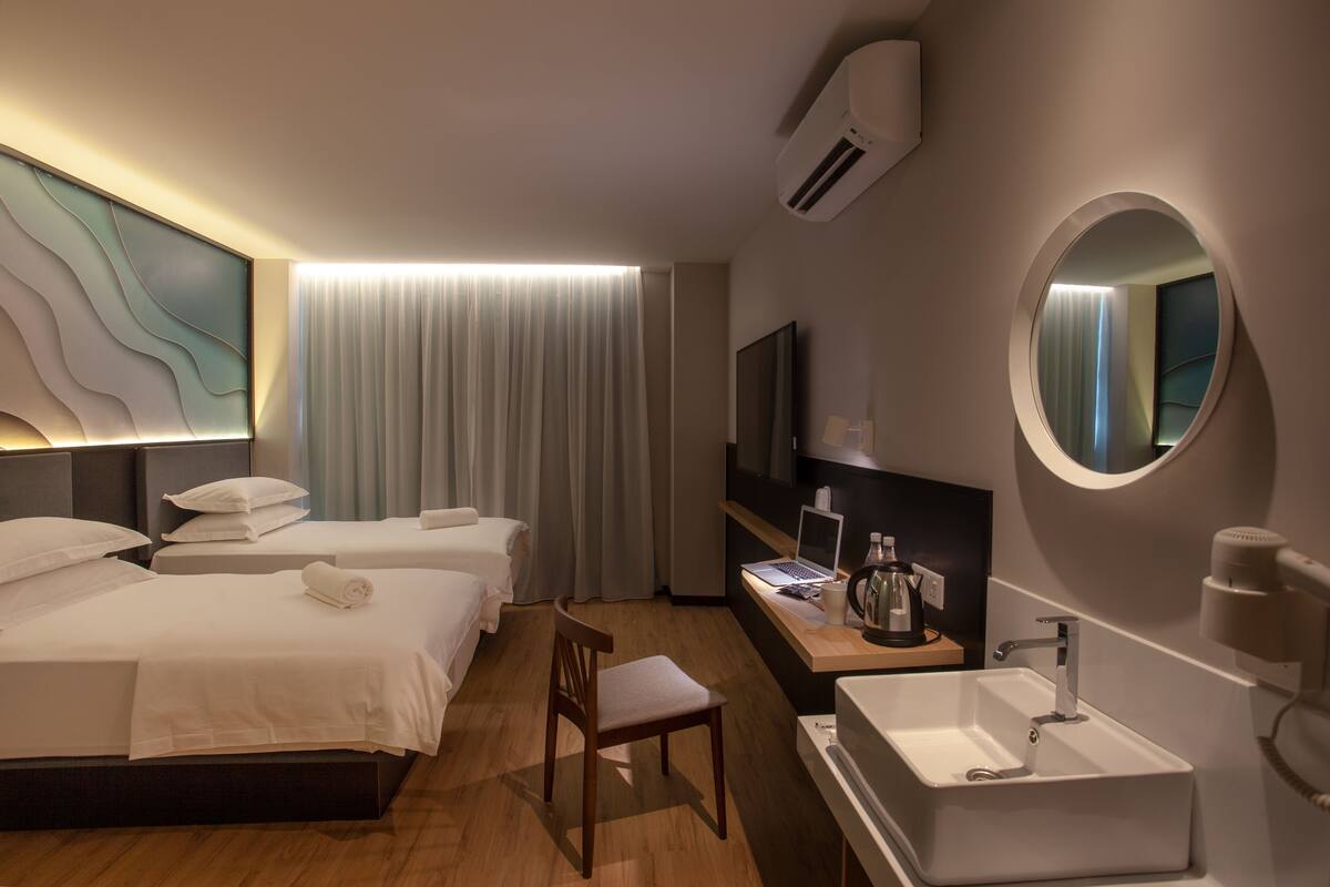 Ein Hotelzimmer mit zwei Betten, einem Schreibtisch mit einem Laptop, einem Waschbecken und einem Spiegel.