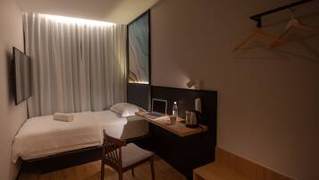 A hotel room with a bed, desk, chair, and a TV mounted on the wall.