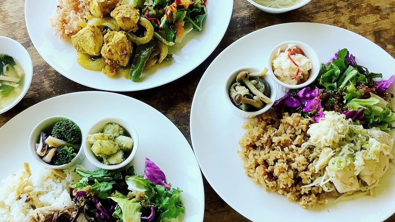 A table with four plates of food, each containing rice, vegetables, and a small bowl of sauce.