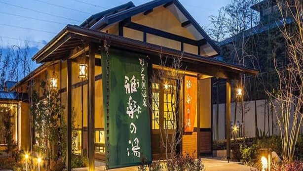 Un edificio tradicional japonés con un gran cartel verde, fachada de madera y una entrada bien iluminada.