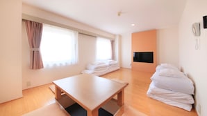 Una habitación de hotel con piso de madera, una cama con sábanas blancas, un televisor de pantalla plana montado en la pared y una mesita de noche.