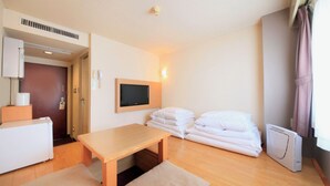 Habitación de hotel con una mesa de madera, televisor montado en la pared, cama con ropa blanca, calentador y ventana con cortinas.