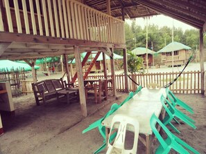 An outdoor dining area with wooden tables and chairs, a covered seating area, and a fenced perimeter. - Camp Rofelio Surfing Beach Resort (San Felipe)