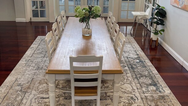 A spacious dining area with a long wooden table and white chairs, a vase of flowers, and large windows offering a view of the outdoors. - SPEERS POINT - Water Views, Pool, Sleeps 12, 8 Beds, Great for Families/groups (Speers Point)