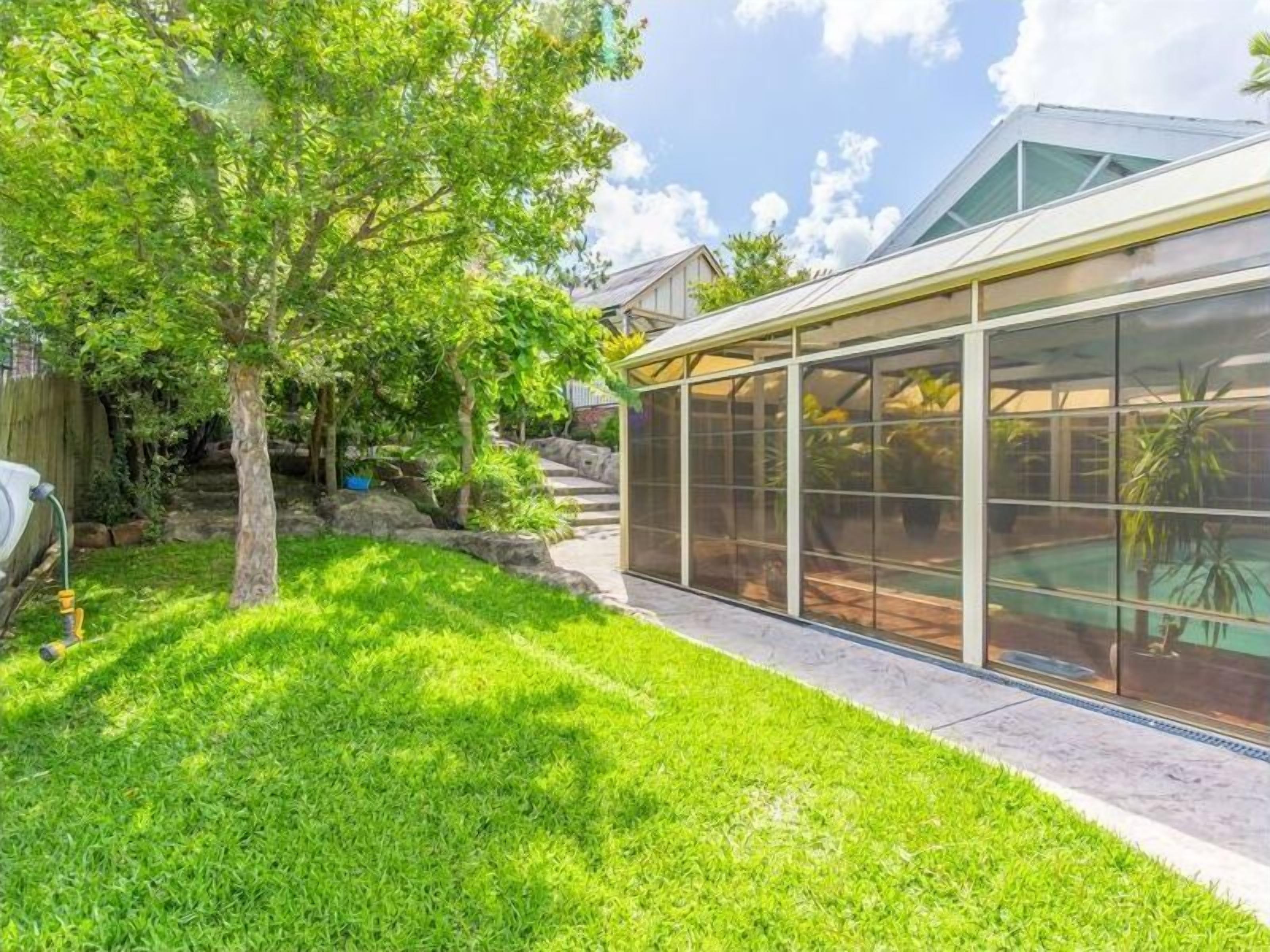A greenhouse with a glass enclosure, a well-maintained lawn, and a tree.