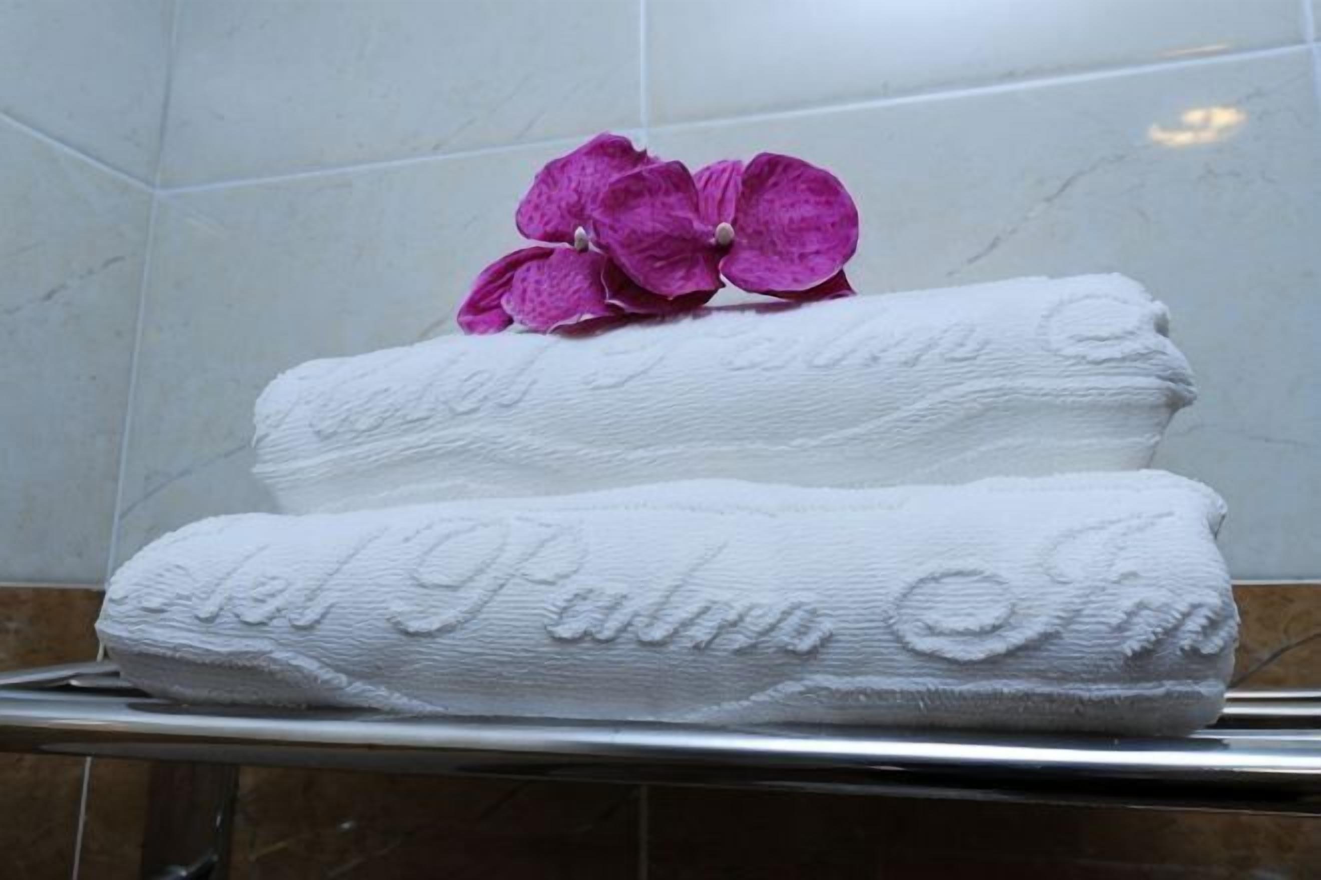 Zwei weiße Handtücher mit geprägtem Text und einer violetten Blume auf einer Badezimmerablage.