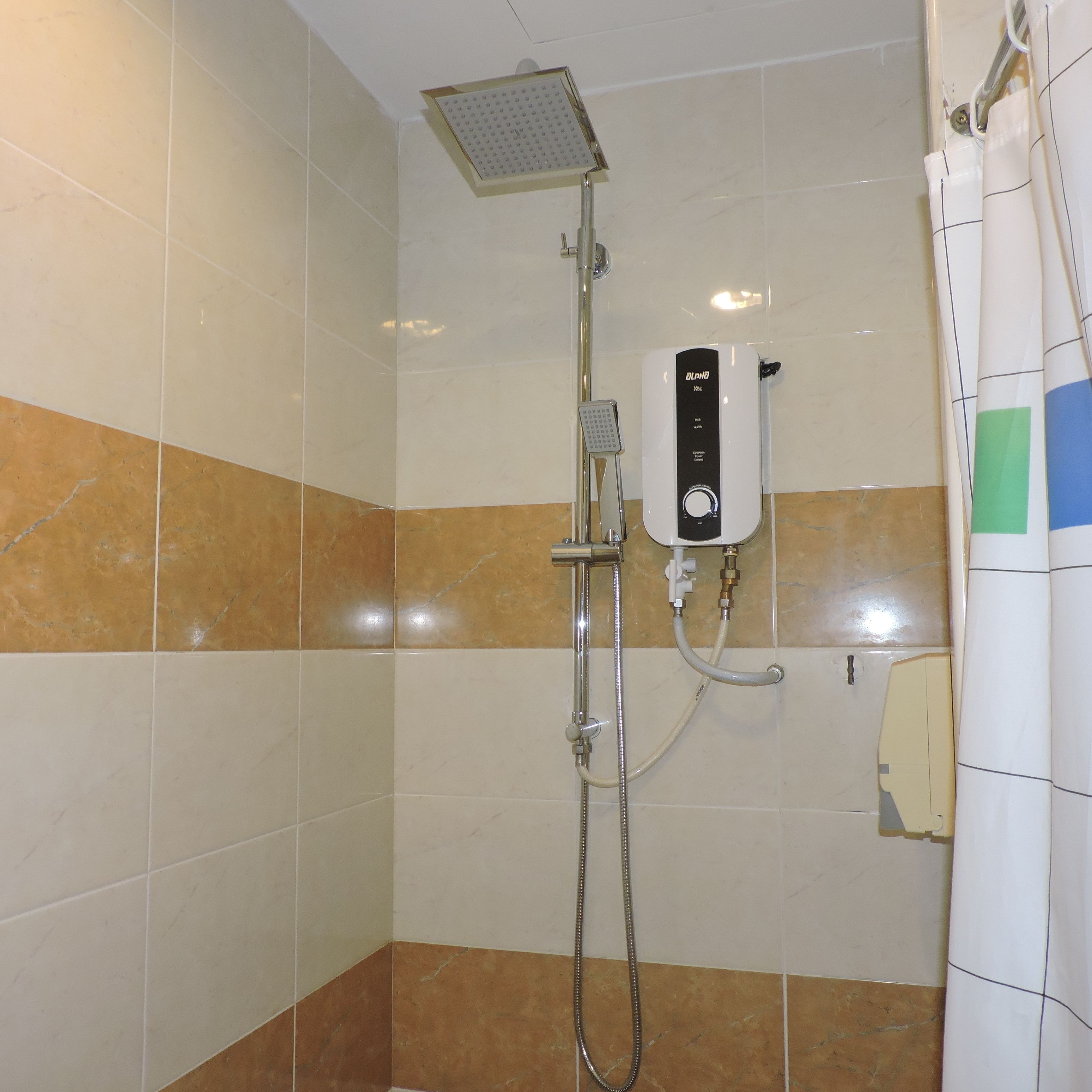 Een douche met een handdouche, een bedieningspaneel aan de muur en een douchegordijn.