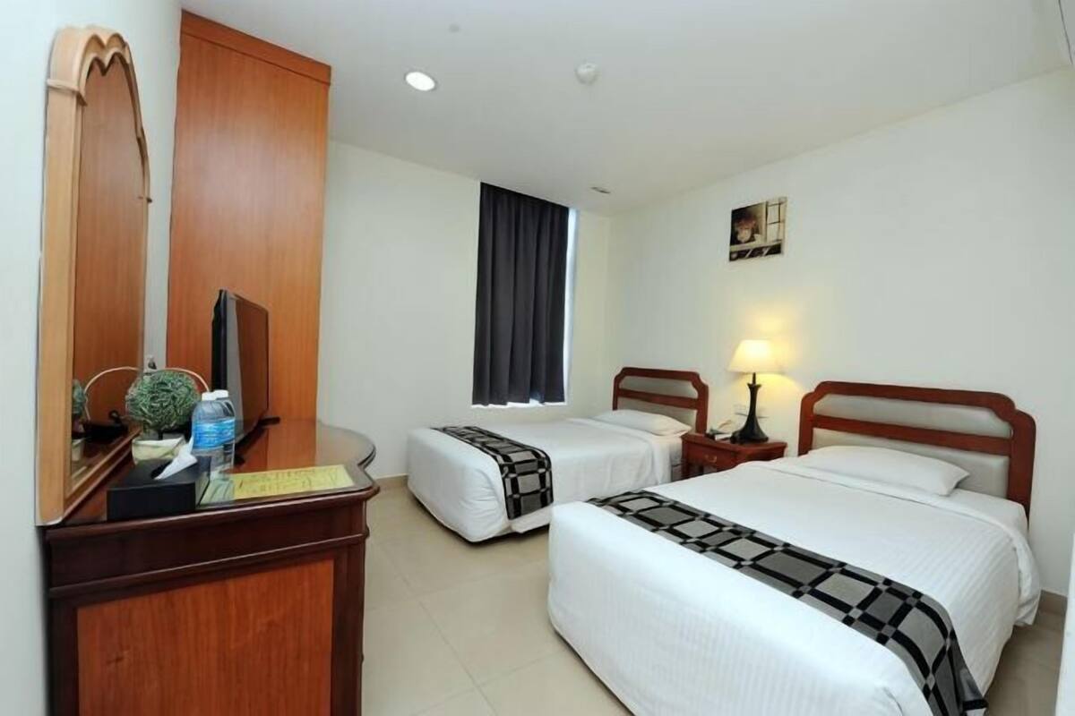 A hotel room with two beds, a desk with a computer, a mirror, and a window with curtains.