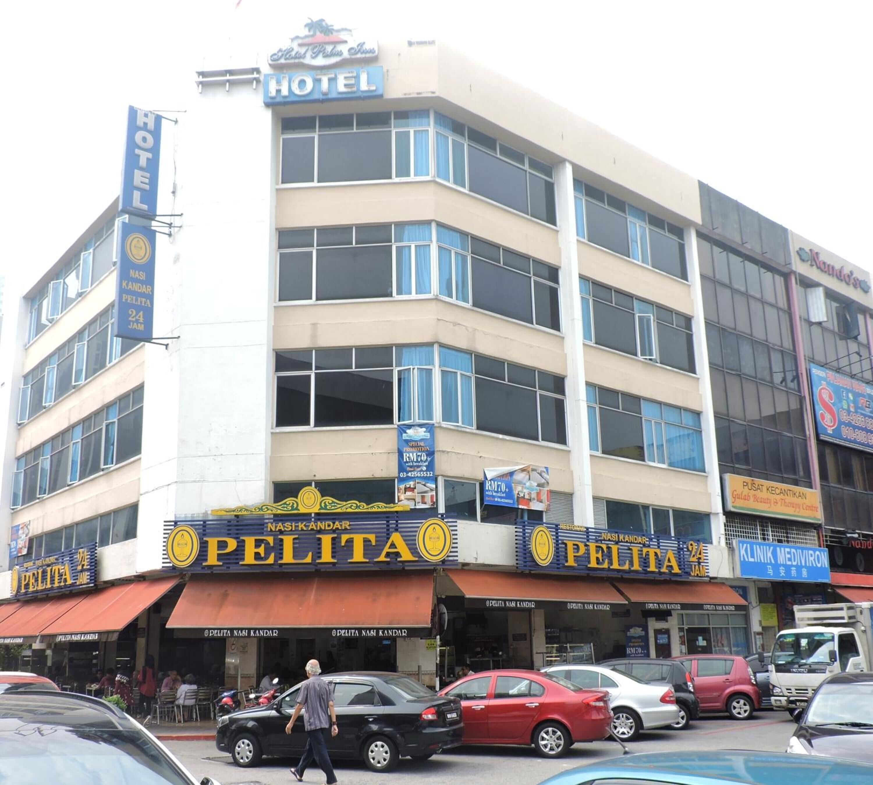 Un edificio de varios pisos con un letrero de hotel en la parte superior, varios locales comerciales en la planta baja y una calle concurrida en frente.