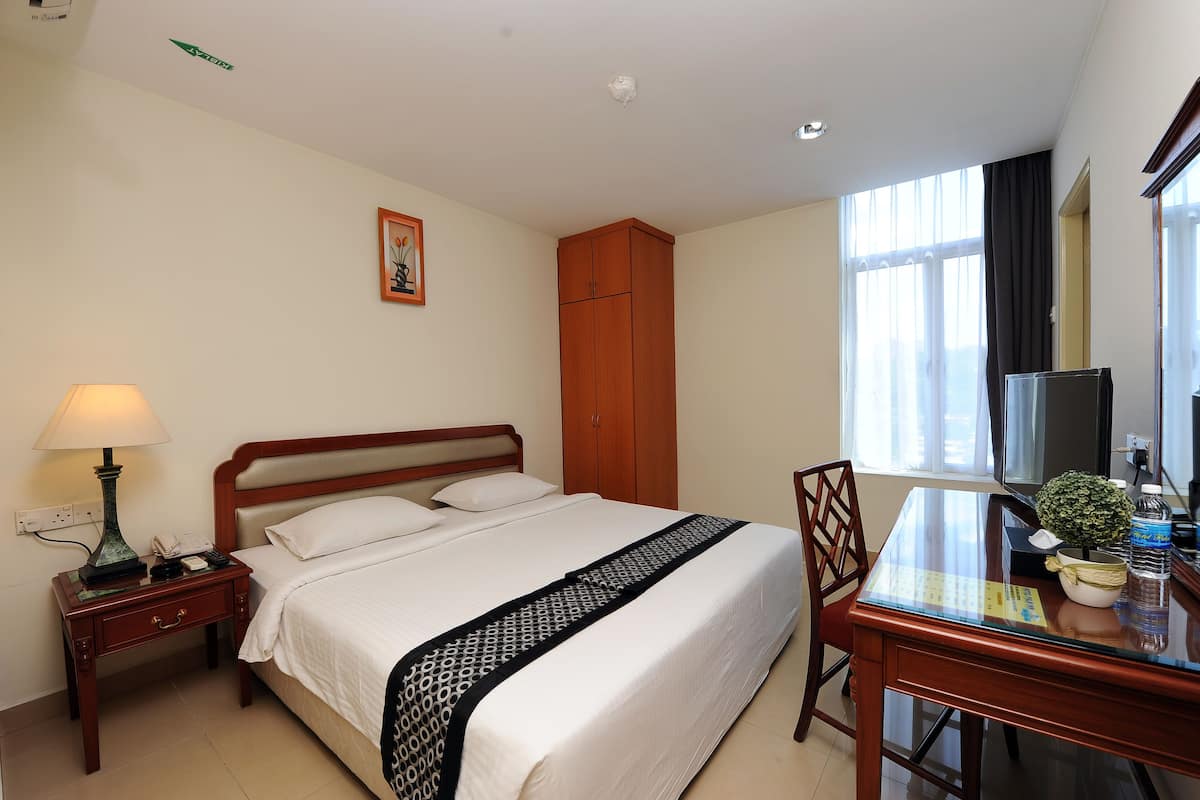 A hotel room with a bed, bedside table, lamp, desk, chair, and a window with curtains.