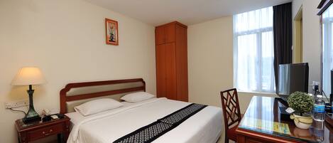 Habitación de hotel con cama, mesita de noche, lámpara, escritorio, silla y ventana con cortinas.