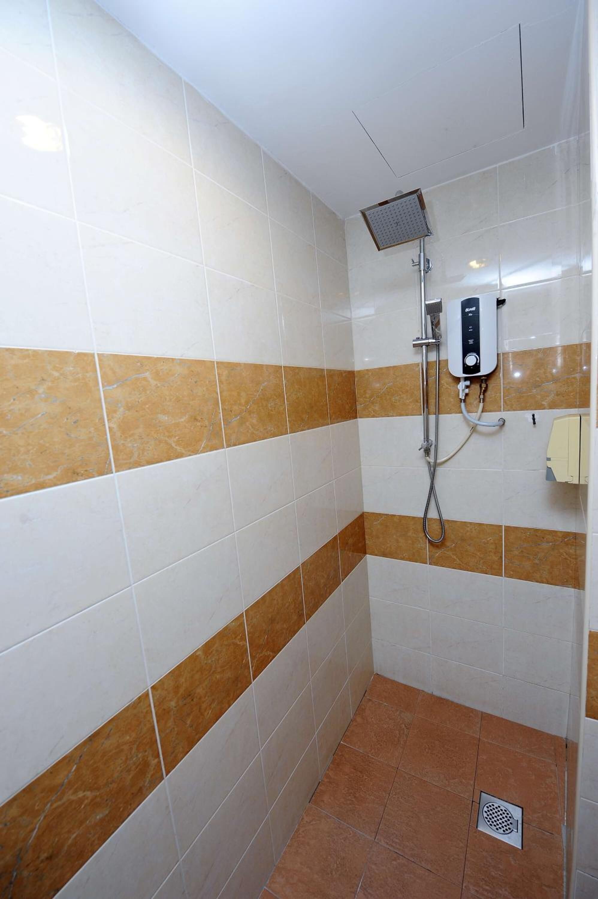 Une salle de bain avec des carreaux blancs et bruns, une pomme de douche et un sèche-mains.