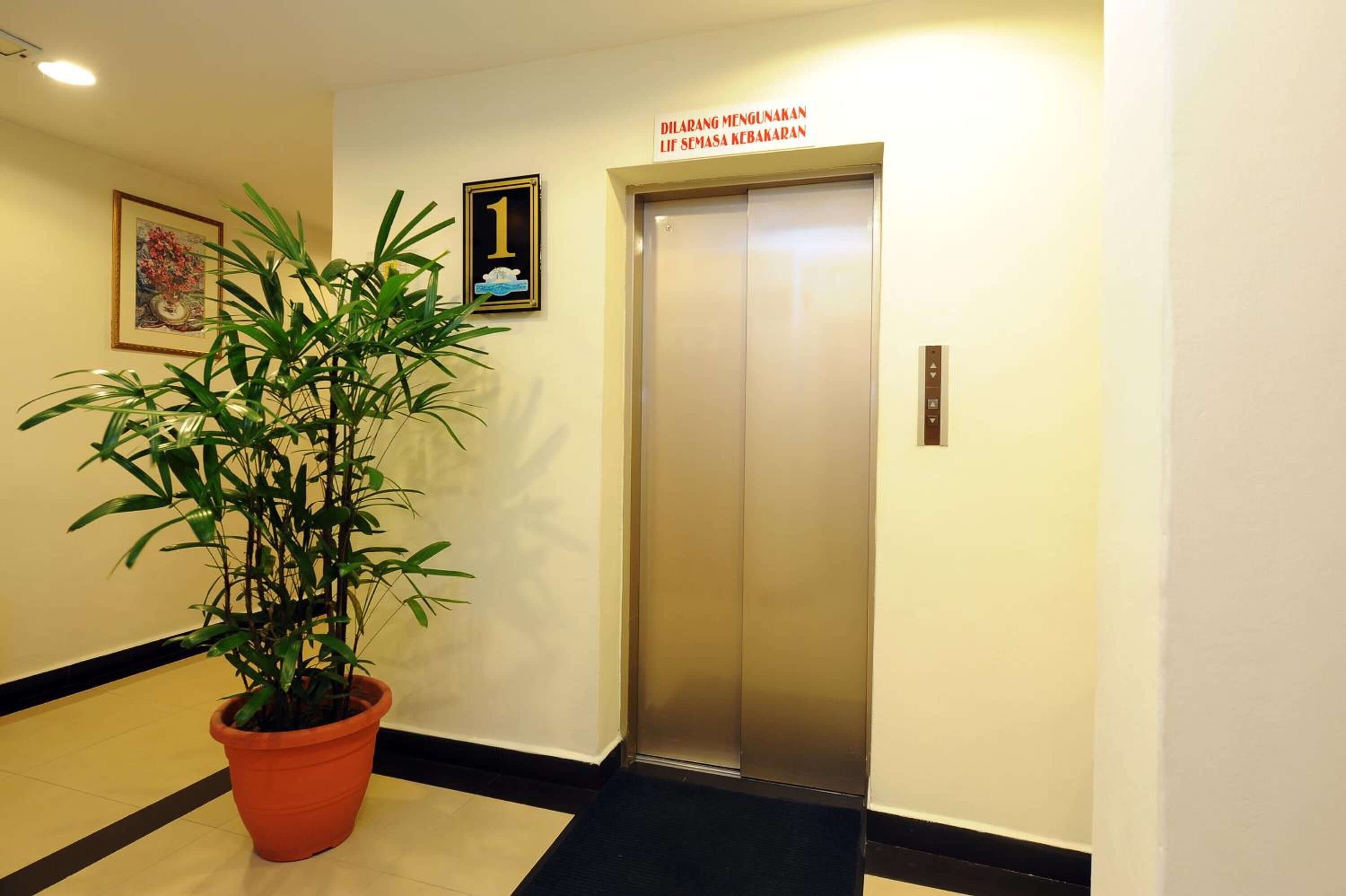 Un ascensor con un cartel encima, una planta en maceta y un cuadro en la pared.