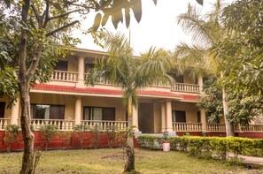 A two-story building with a red-tiled roof, a balcony on each floor, and a well-maintained garden with various trees and shrubs. - Nadiya Parao Resort, Corbett (Ramnagar)