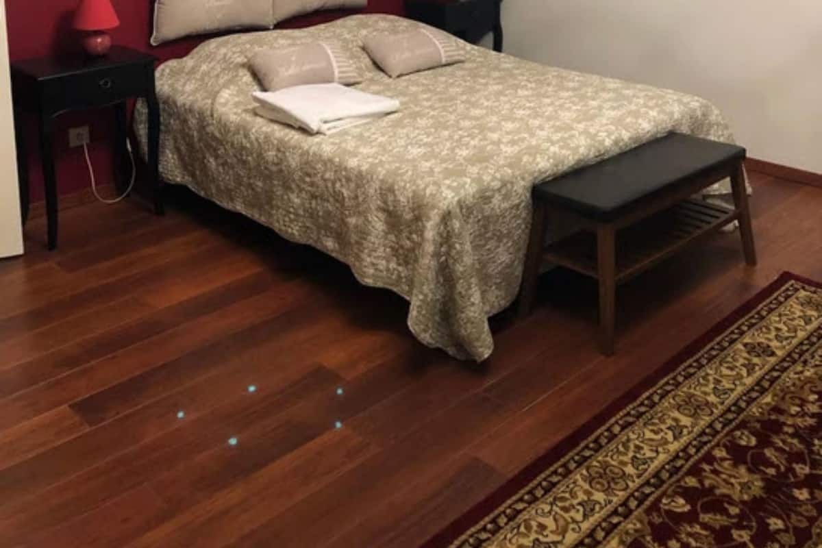 A bedroom with a bed, bedside tables, a bench, a chandelier, and two paintings on the walls.