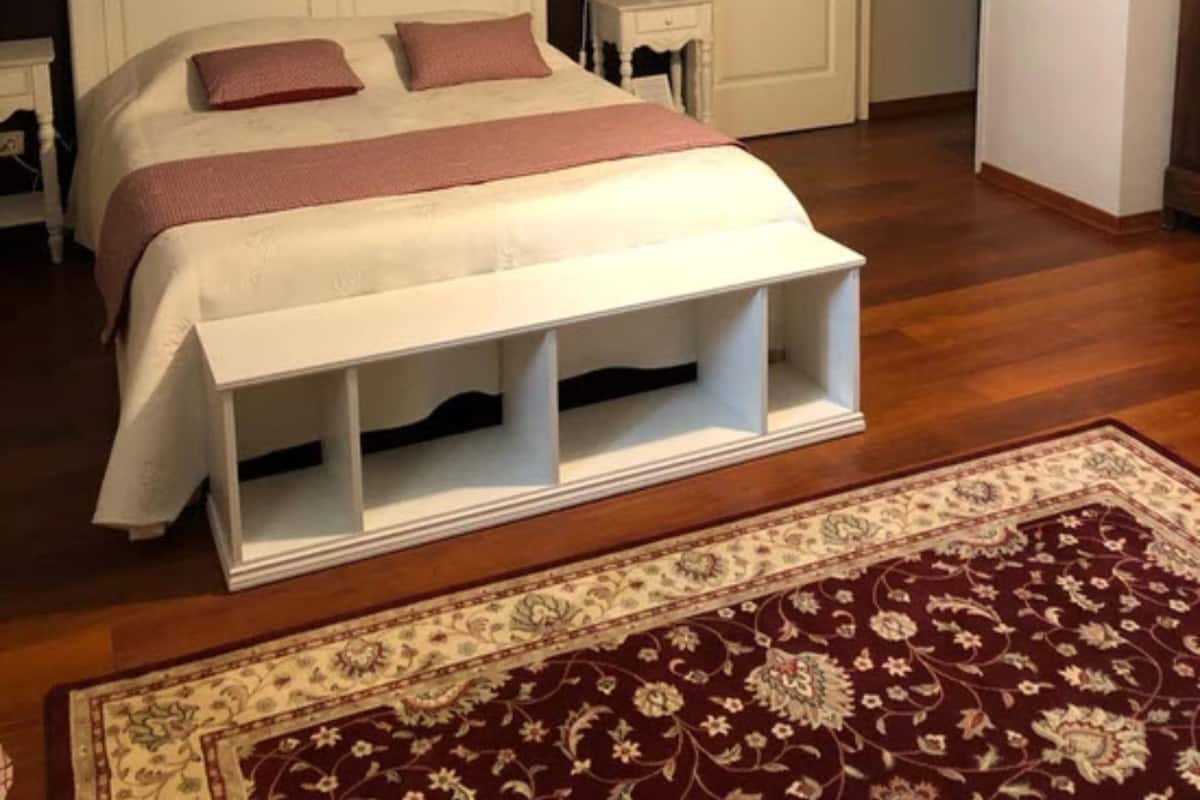 A bedroom with a white bed, a wooden floor, a dark wall with artwork, a white door, and a patterned rug.