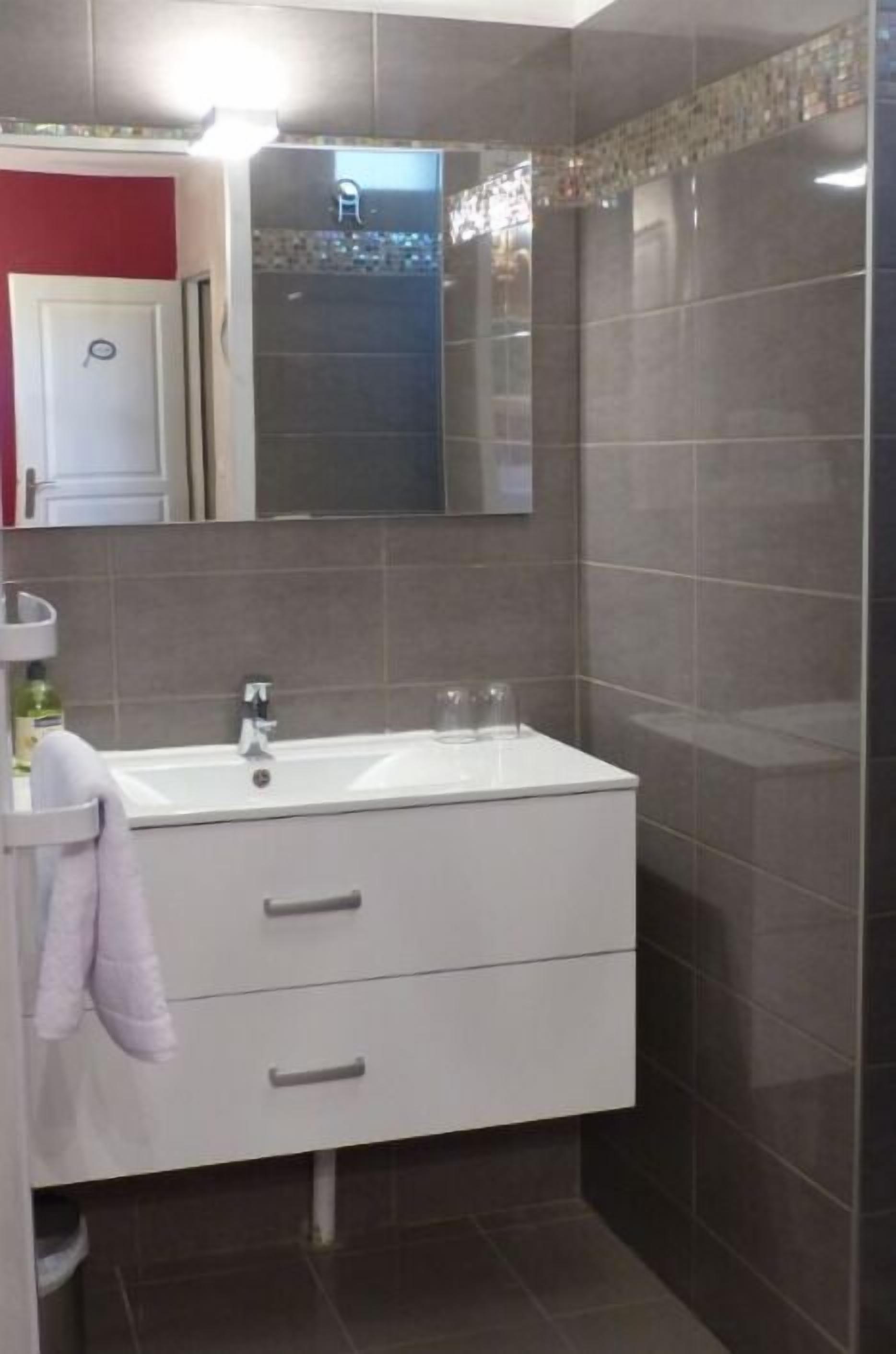 Ein Badezimmer mit weißem Waschtisch, einem Spiegel und einer Duschkabine.