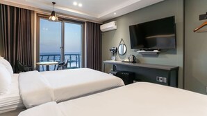 A hotel room with two beds, a TV, a desk with a mirror, and a view of the sea. - Hotel Juno (Gangneung)