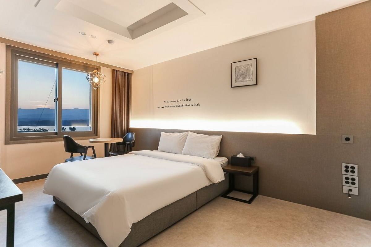 A modern hotel room with a large bed, a desk, a chair, and a view of the mountains.