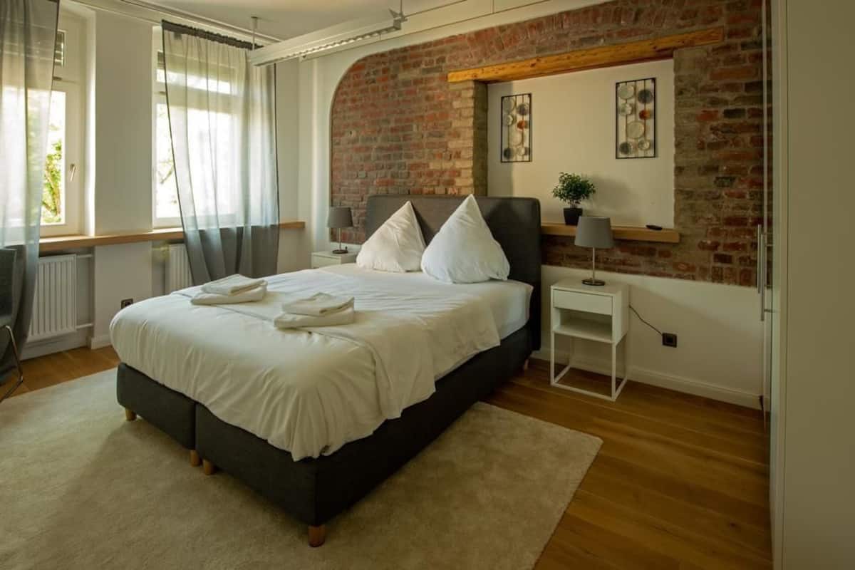 Une chambre à coucher avec un lit, une table de chevet, une lampe, une plante et un mur en briques.