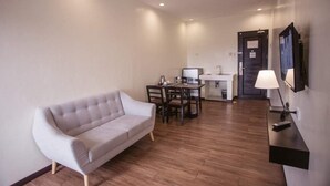 A modern hotel room with a sofa, a dining table with chairs, a small kitchen area, and a TV mounted on the wall. - Piña Suites (Ormoc)