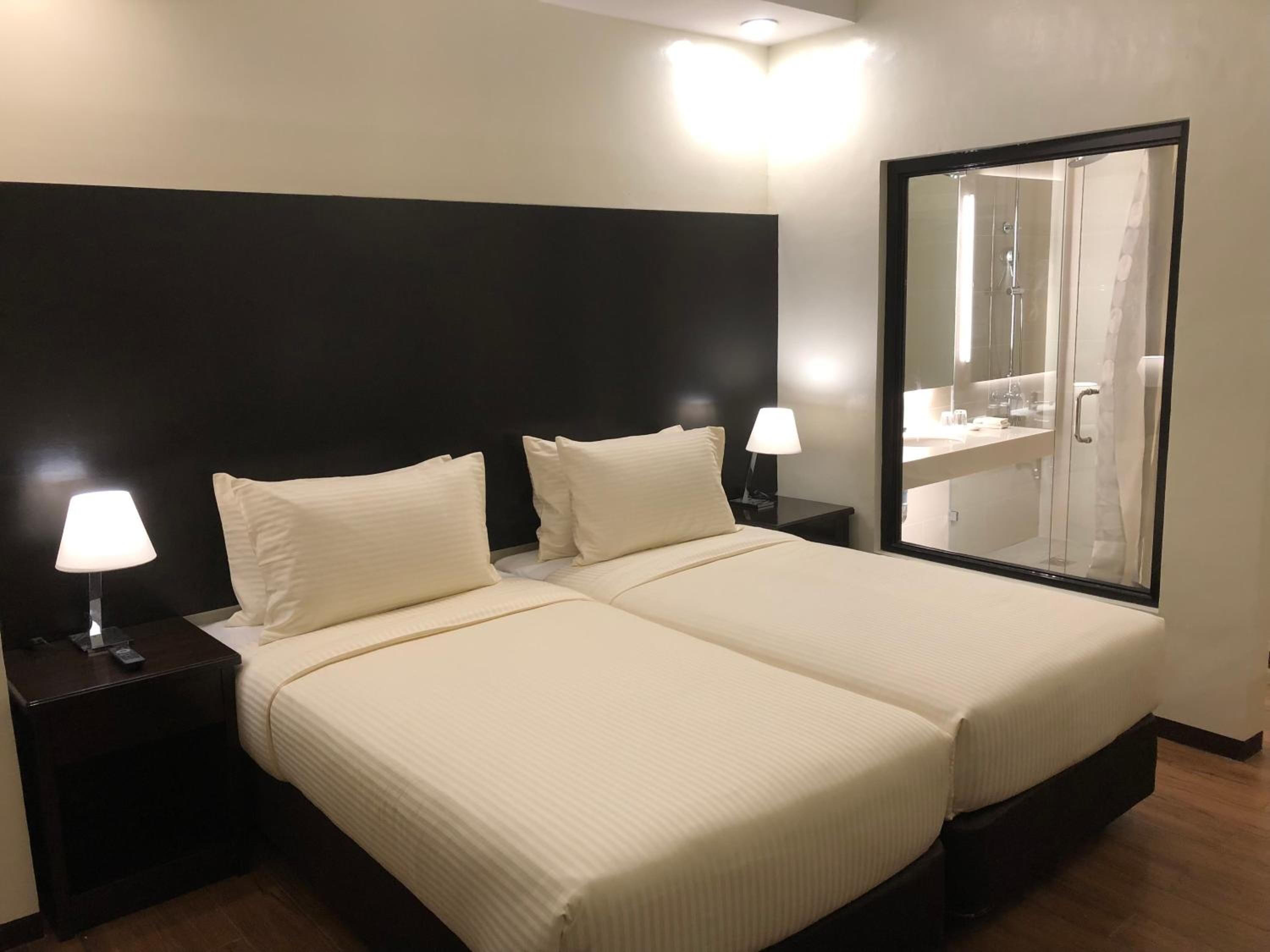 Une chambre d’hôtel avec un lit double, deux lampes de chevet, un grand miroir et vue sur la salle de bain.