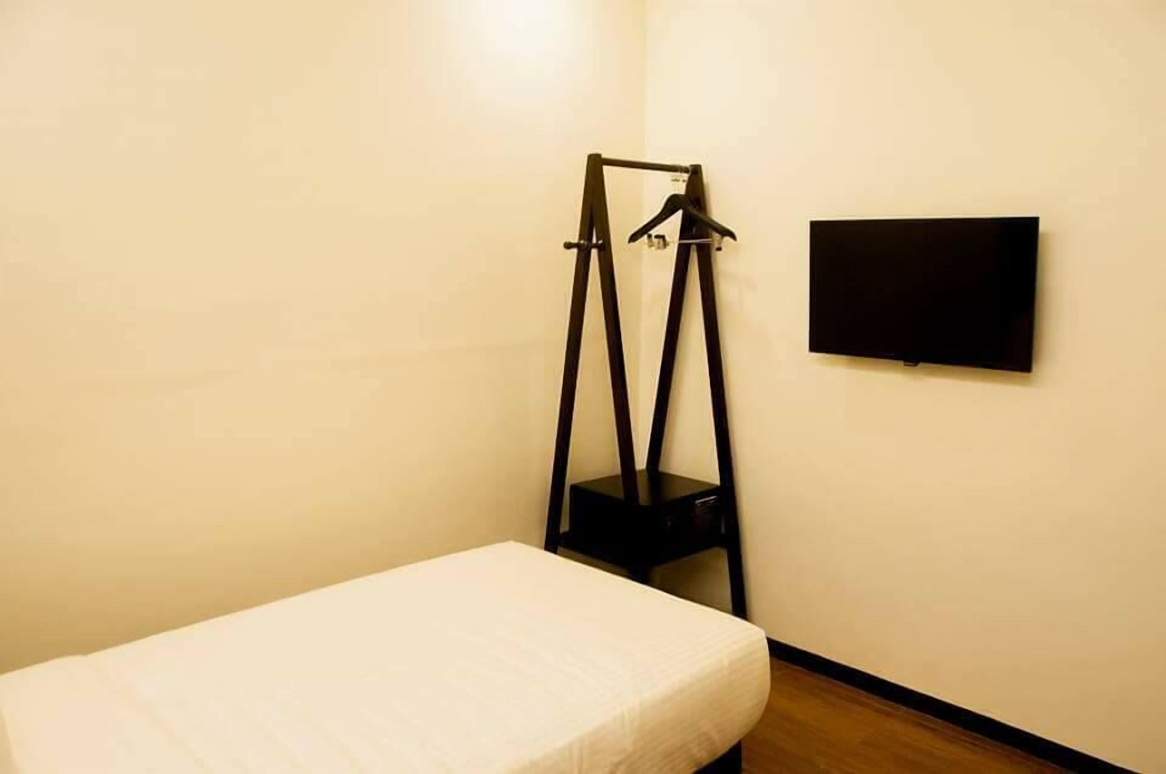 A small room with a bed, a black chair, and a flat-screen TV mounted on the wall.