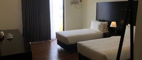 A hotel room with two beds, a desk, a chair, a TV, and an air conditioning unit.
