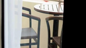 A balcony with a round table and two chairs, a view of a red-roofed building, and a white curtain partially obscuring the view. - Piña Suites (Ormoc)