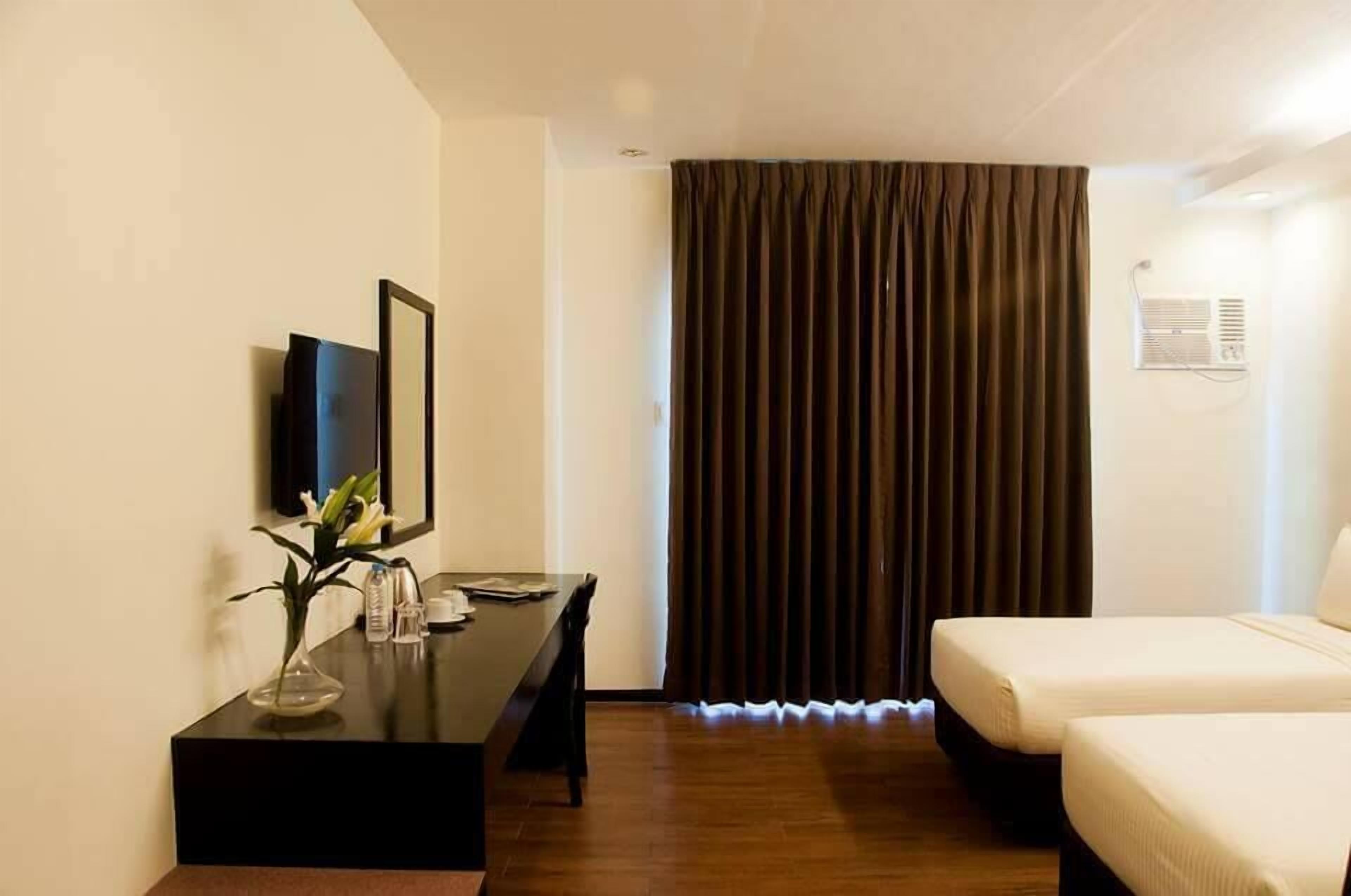 A hotel room with a bed, a desk with a vase of flowers, a mirror, and a window with curtains.