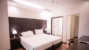 A hotel room with a large bed, two bedside tables with lamps, a desk, and a mirror. - Piña Suites (Ormoc)
