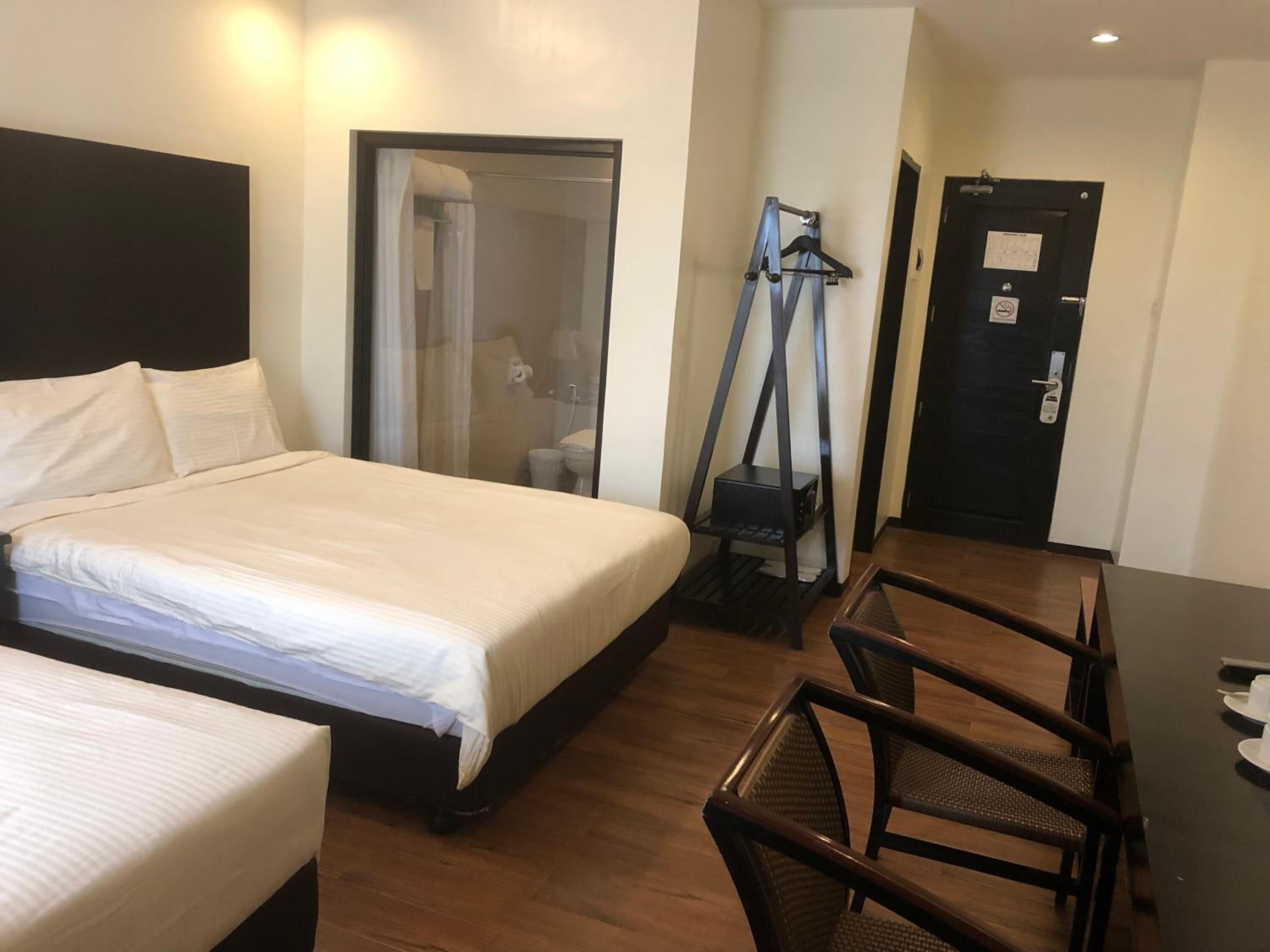 A hotel room with a large bed, a desk with chairs, a shower area, and a door with a sign.