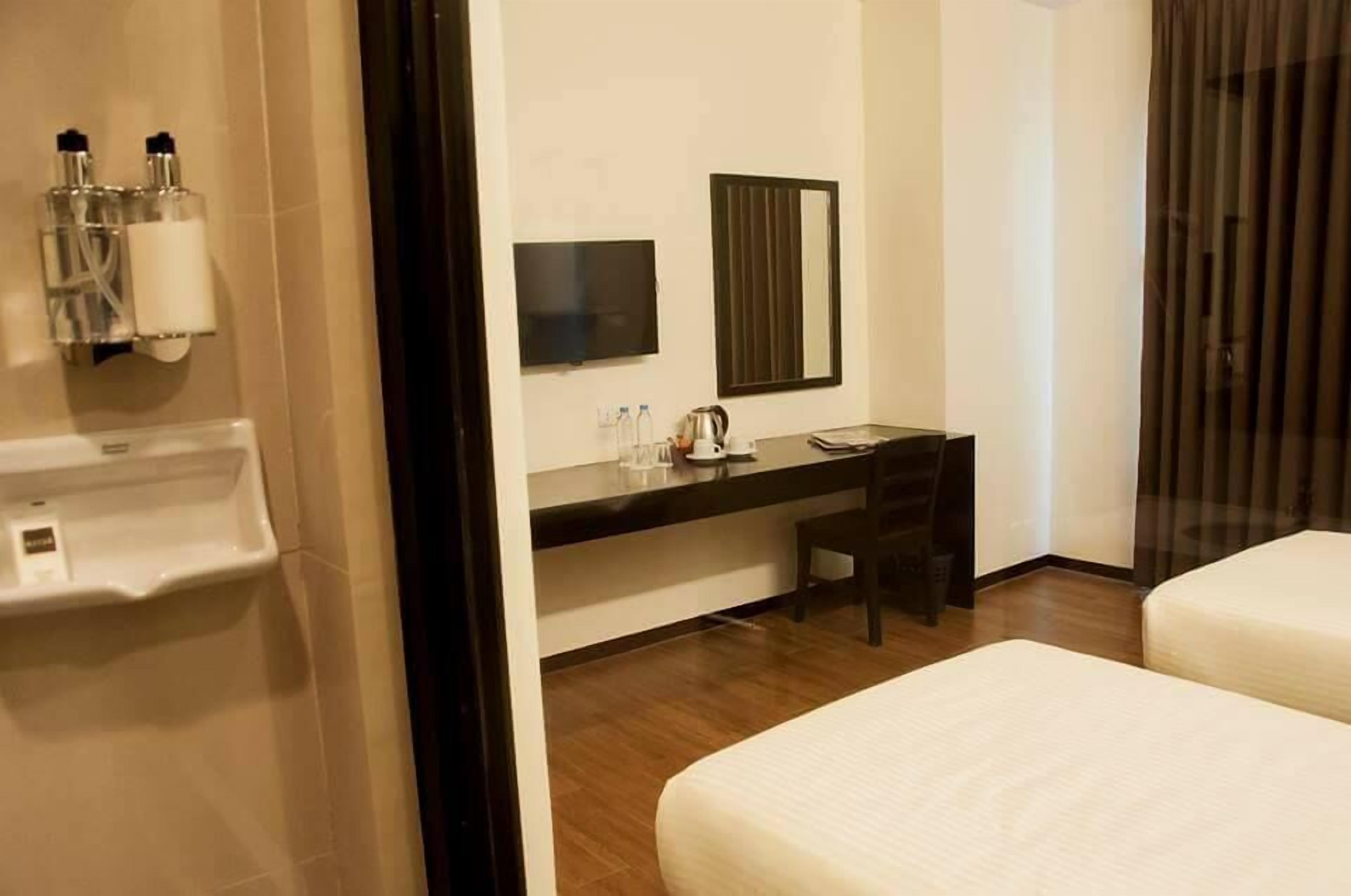 Ein Hotelzimmer mit Schreibtisch, zwei Betten, Fernseher und Spiegel.