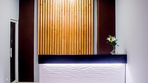 A reception area with a wooden slatted wall, a white reception desk, and a ceiling light. - Piña Suites (Ormoc)