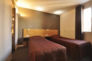 Una habitación con dos camas individuales, cabecera de madera, mesita de noche pequeña y ventana con cortinas.