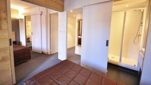 A modern hotel room with a wooden ceiling, a large bed, a shower area, and a separate bathroom. - Hôtel de l'Europe et des Bains (Monetier-les-Bains)