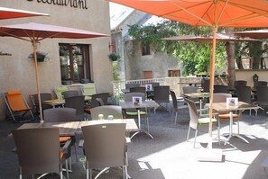Un café al aire libre con mesas y sillas, algunas con sombrillas.