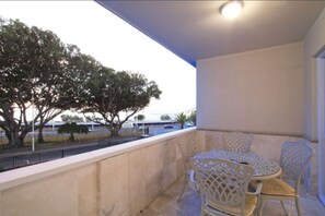 A balcony with a table and chairs, a view of trees and a parking lot.