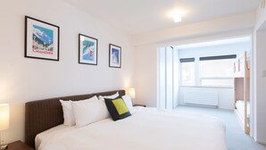 A hotel room with a large bed, a nightstand, a lamp, and a window with a view. There are three framed pictures on the wall. - Ajisai Chalet  (Kutchan)