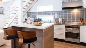 A modern kitchen with a central island, wooden chairs, a stainless steel range hood, and a tiled backsplash. - Ajisai Chalet  (Kutchan)