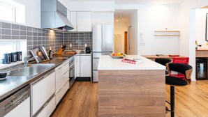 A modern kitchen with white cabinets, a stainless steel countertop, and a wooden dining area with bar stools. - Ajisai Chalet  (Kutchan)