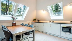Une cuisine moderne dotée de fenêtres de toit, un coin repas avec une table et des chaises en bois, et une vue sur les arbres par les fenêtres.