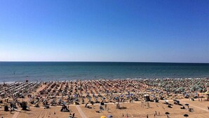 Een druk strand met veel parasols en badgasten.